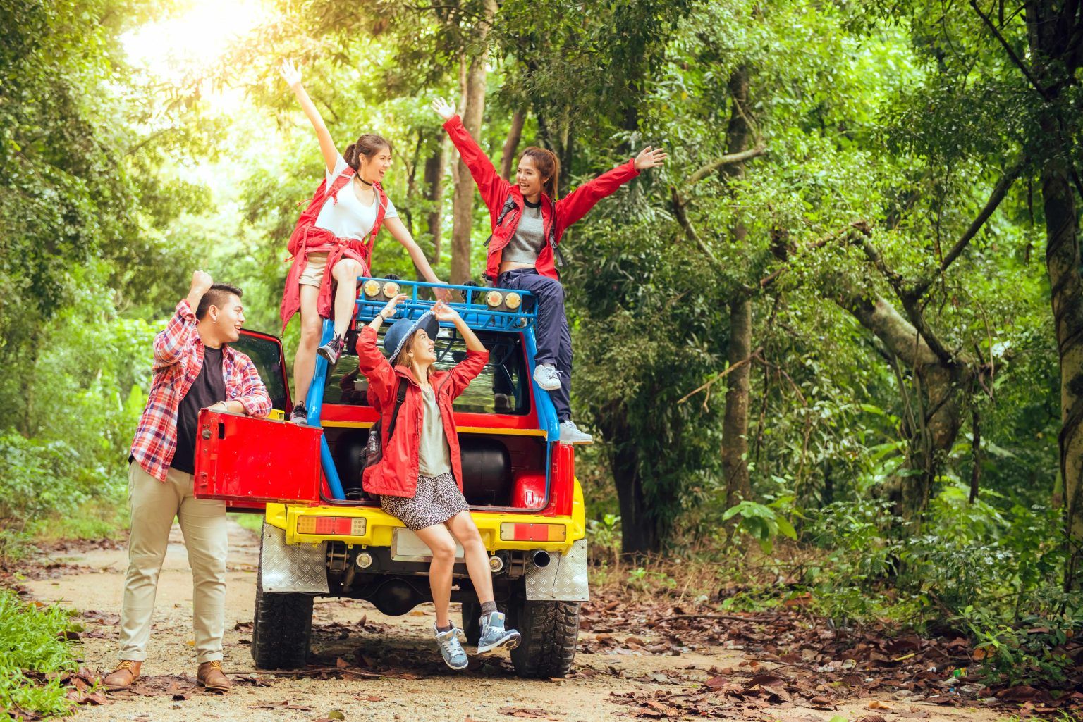 Four excited hikers celebrate on a colorful utility vehicle in a sunny forest.